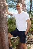 Mann mit grauen Haaren in weißem T-Shirt und dunkelblauer Shorts im Wald