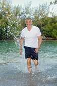 Mann mit grauen Haaren in weißem T-Shirt und dunkelblauer Shorts rennt durch Wasser