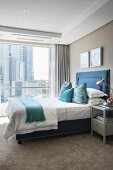 Bed with upholstered blue frame and beige carpet in elegant bedroom