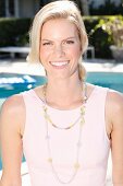 A blonde woman wearing a pink dress and a necklace in front of a pool