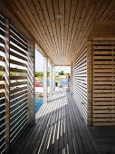 Slatted wooden arcade surrounding floating wooden house; pattern of light and shade