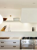 White wall-mounted shelves, indirect lighting and gas hob in kitchen