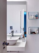 Einblick in Bad mit weißem Waschtisch, Wandspiegel und aufgehängten Glasregalen