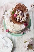 A naked sponge cake decorated with an Easter nest, chocolate eggs, and blossoms