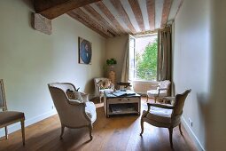 Antique armchairs in lounge area with large open window and rustic wood-beamed ceiling