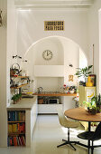Runder Tisch, Klassikerstühle, Küchenzeile mit Betonplatte und mobiler Gasherd in der Küche mit Rundbogen