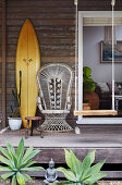 Surfboard, peacock chair and swing on vintage porch of a wooden house