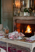 Table set for afternoon coffee in front of roaring fire in open fireplace