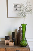 Grass in green vase and letter stamps decorating chest of drawers