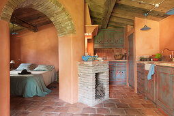 Mediterranean kitchen with terracotta tiles, fireplace and view into bedroom through open arched doorway