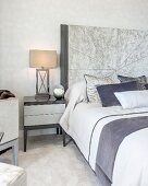 Bedside lamp on cabinet next to bed with tall headboard in elegant bedroom in shades of grey