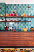 Colourful crockery in kitchen with wooden cupboards and blue retro wall tiles