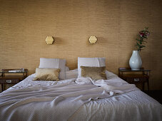 Double bed, bedside tables and lamps mounted on wall covered in elegant wallpaper