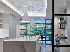 Glass and steel partition wall and marble island counter in modern kitchen
