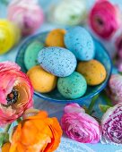 Colourful speckled eggs in bowls amongst ranunculus flowers