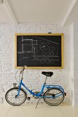 Blue folding bike below architect's plan on chalkboard