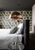 Copper-coloured ceiling lamps above bed in front of patterned wallpaper