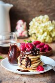 A stack of pancakes with chocolate sauce and raspberries