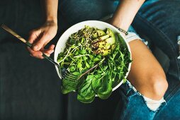 Green vegan breakfast meal in bowl with spinach, arugula, avocado, seeds and sprouts