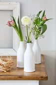 Ranunculus, tulips and gypsophila in three white bottles
