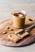 Almond and cinnamon butter on a slice of rye bread with a knife and a glass jar of almond and cinnamon butter in the background