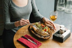 A woman eating grilled mackerel and vegetables on a wooden board