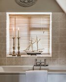 Candlesticks and model boat in front of louvre blinds on windowsill of bathroom window