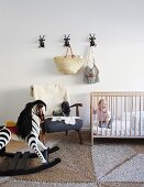 Toddler in cot next to sheepskin on retro armchair and rocking horse