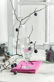 Blackthorn schnapps in a glass, blackthorn fruits in a storage jar and a blackthorn branch on a kitchen table