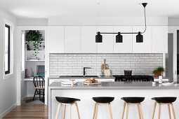 Fitted kitchen with subway tiles, kitchen counter with bar stools and black light in an open living room