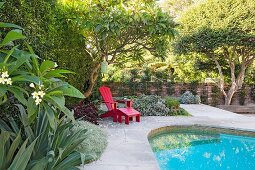 Roter Deckchair am Pool im sommerlichen Garten