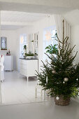 Simple Christmas tree in basket in dining room decorated entirely in white
