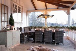 Dining table and faux-wicker chairs on rustic veranda with winter decorations