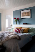 Fur blanket on bed against blue wall panel in bedroom