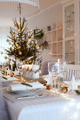 Stimmungsvoll gedeckter Tisch mit Nadelzweigen und Lichterkette an Weihnachten