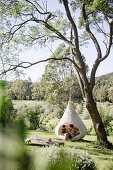 Mother and daughter sit in the hanging chair in the garden