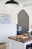 View over vintage kitchen island to white wooden paneling with sign next to pointed arch passage in former church