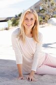 Blonde Frau in beigefarbenem Langarmshirt und rosafarbener Hose am Strand