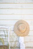 Straw hat hung on clapboard wall next to chair
