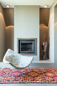 Designer armchair on patterned rug in front of fireplace