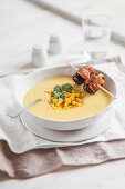 A bowl of creamy corn soup garnished with a date and bacon skewer