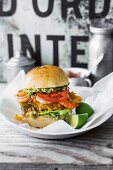 A crispy chicken burger with guacamole, shrimps, pineapple salsa and tomato slices