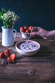 Woman eating strawberry banana smoothie bowl topped with coconut and cacao nibs