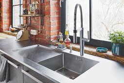 A stainless steel sink in front of a window and a brick wall