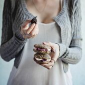 Frau hält selbstgebackene Sandwich-Cookies mit Brombeeren und Frischkäse in den Händen