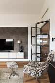 Sessel mit passendem Fusshocker in elegantem Wohnhzimmer, offene Glastür, Fernseher auf Hängeschrank
