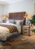 Schlafzimmer mit Betthaupt aus Leder, Überseekoffer als Nachtkästchen und Tierfellteppich