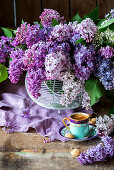 Cup of coffee in front of bouquet of purple lilac