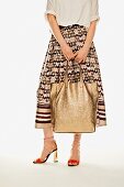 A woman wearing a midi-skirt, a golden leather shopper and ankle tie sandals