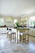 Elegant island counter with white stools on large stone flags in kitchen in French country-house style